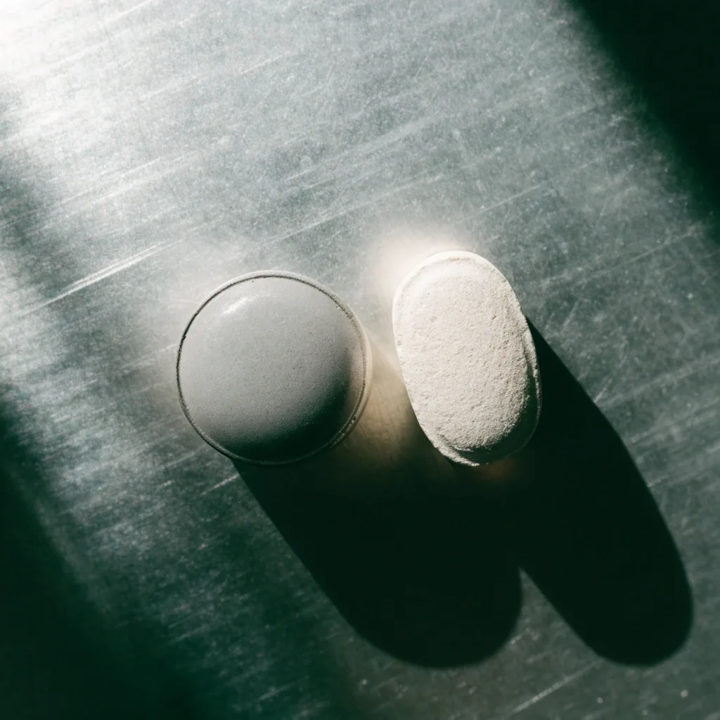 Two tablets of different shapes side by side on a bare metal surface under top light